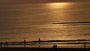 A beach scene with the sun setting over the ocean, silhouettes of people on the shore, and a calm sea. - House in Mimizan, between the lake and the ocean (Mimizan)