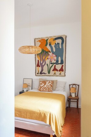 A bedroom with a bed, a hanging light fixture, a wall-mounted painting, and a chair. - Beautiful, bright, and quiet one-bedroom apartment in the heart of the city, near the Old Port (La Ciotat)