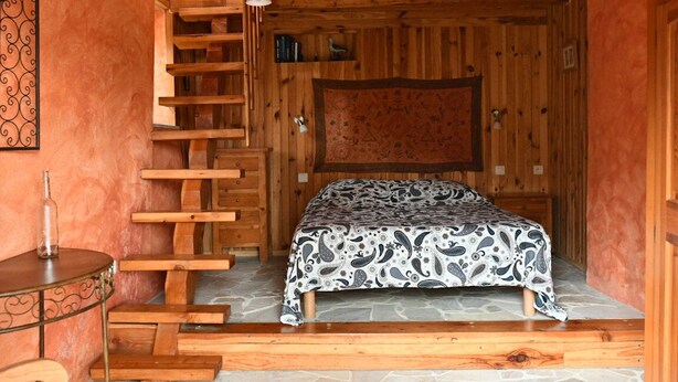 A wooden interior with a bed, a wooden ladder, a table, and a hanging light fixture. - Country cottage (Millau)