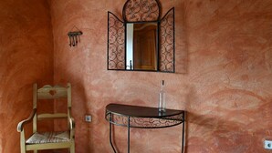 A room with a wooden chair, a small table with a bottle, and a wall-mounted mirror with a decorative frame. - Country cottage (Millau)