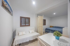 Ein kleiner, hell eingerichteter Raum mit einem Bett, einem weißen Sofa, einem Tisch und einer Topfpflanze.
