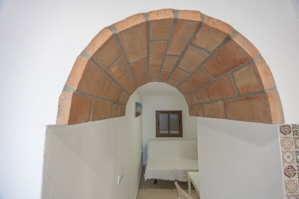 Un corridoio stretto con un arco in piastrelle che conduce a una stanza con un letto e una finestra.