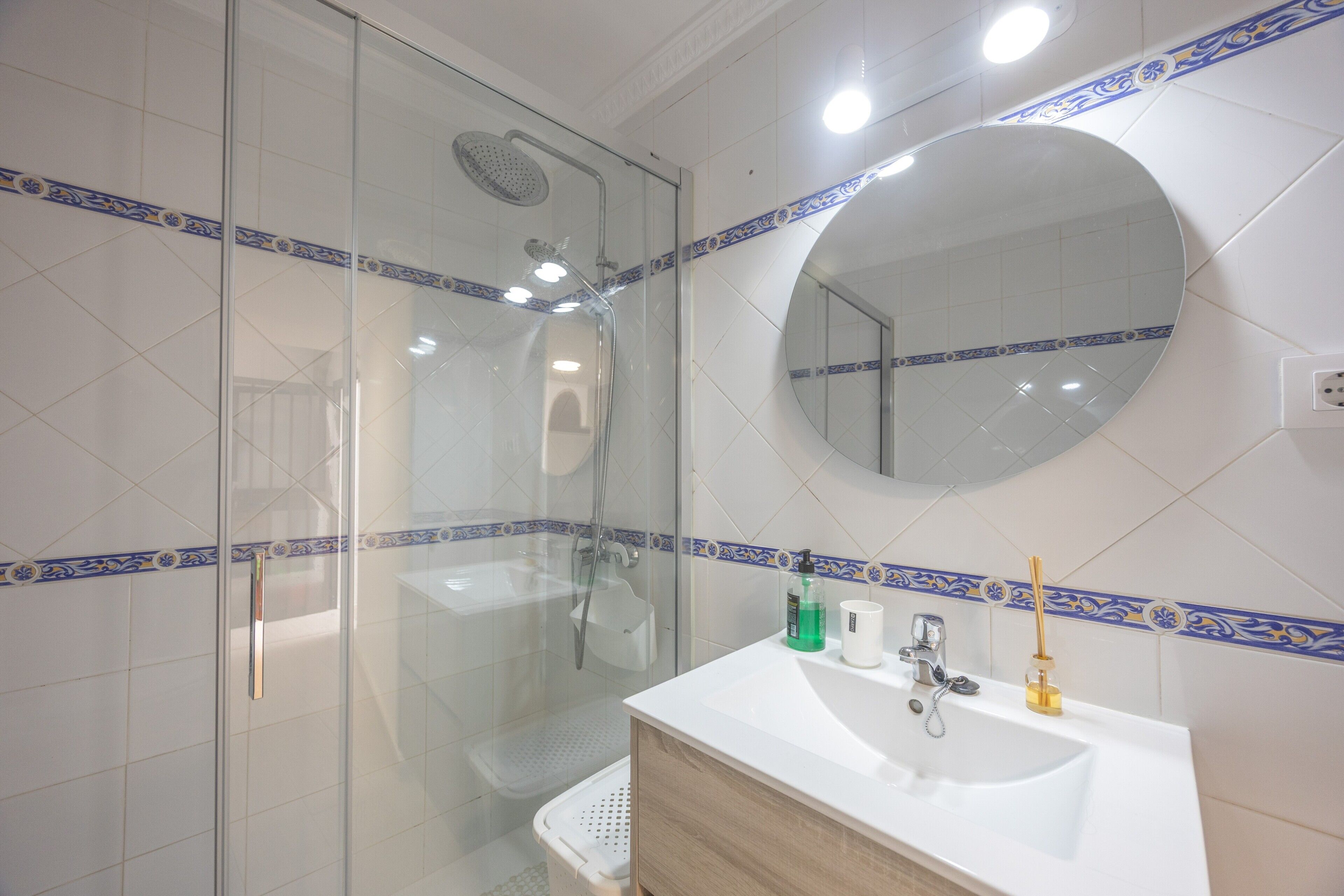 Een badkamer met een douchecabine van glas, een witte wastafel met spiegel en een betegelde vloer.