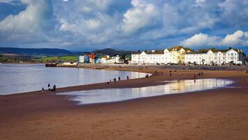 A coastal beach with a row of white buildings, a sandy shore, and a calm sea.
