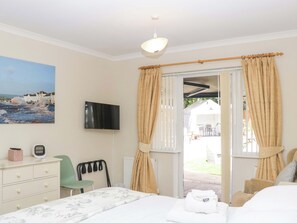 Un dormitorio con cama, televisión, escritorio, silla y vistas al exterior.