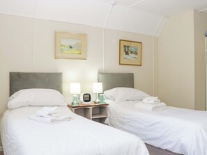 Ein Hotelzimmer mit zwei Betten, einem Nachttisch mit Lampen und zwei gerahmten Bildern an der Wand.
