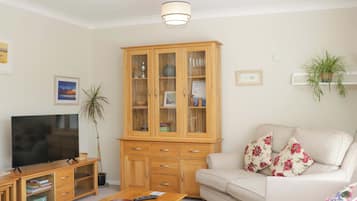 Una sala de estar con televisor, aparador de madera, sofá y una mesita.