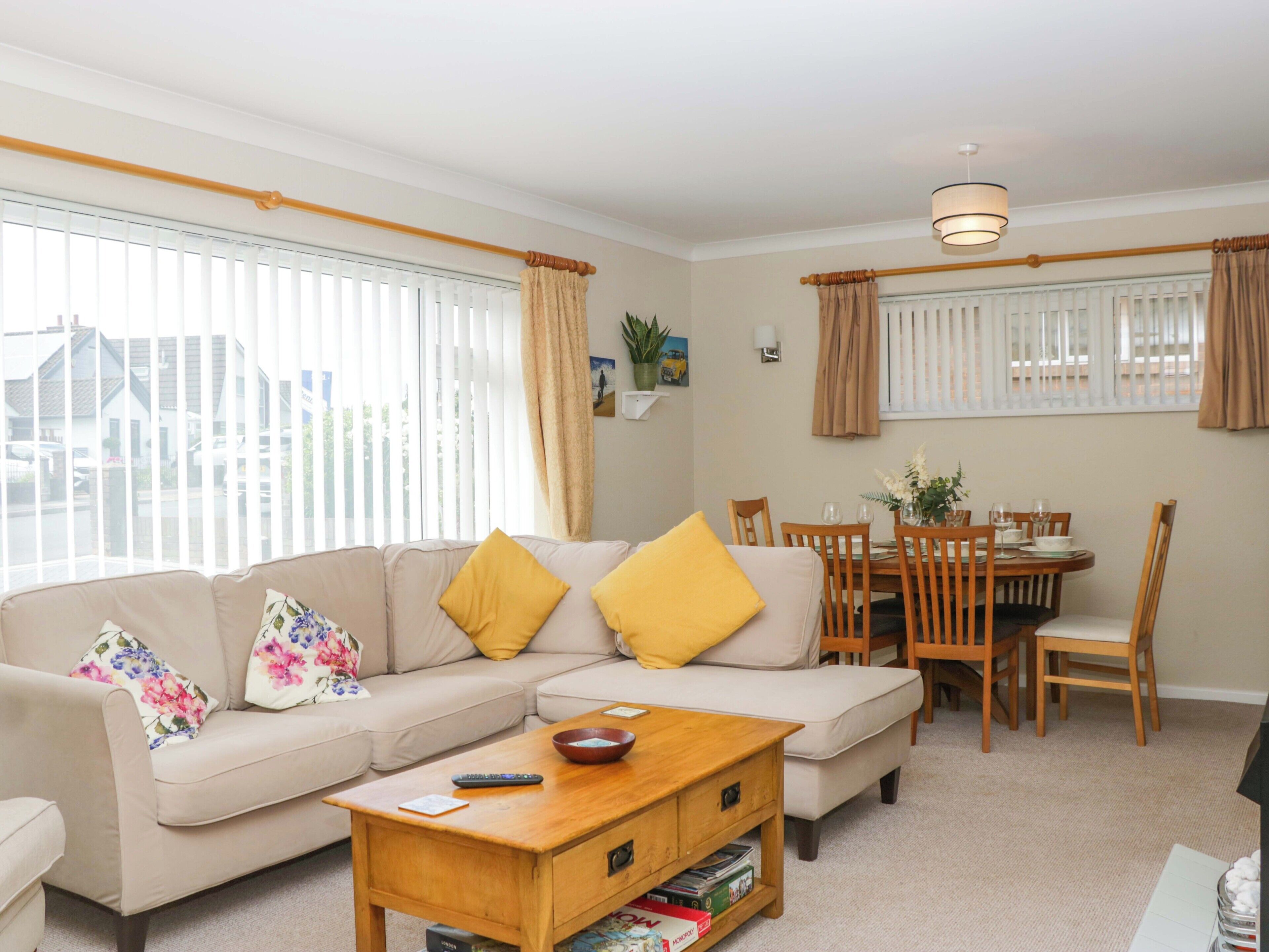 A living room with a sofa, coffee table, dining table, chairs, and a window with blinds.