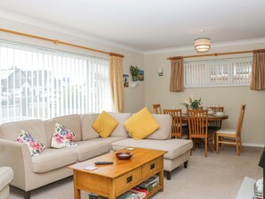 A living room with a sofa, coffee table, dining table, chairs, and a window with blinds.