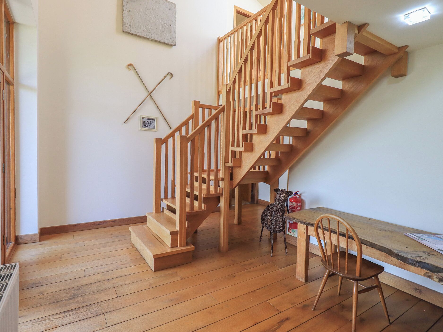 A wooden staircase in a room with a wooden floor, a small table, and a chair.