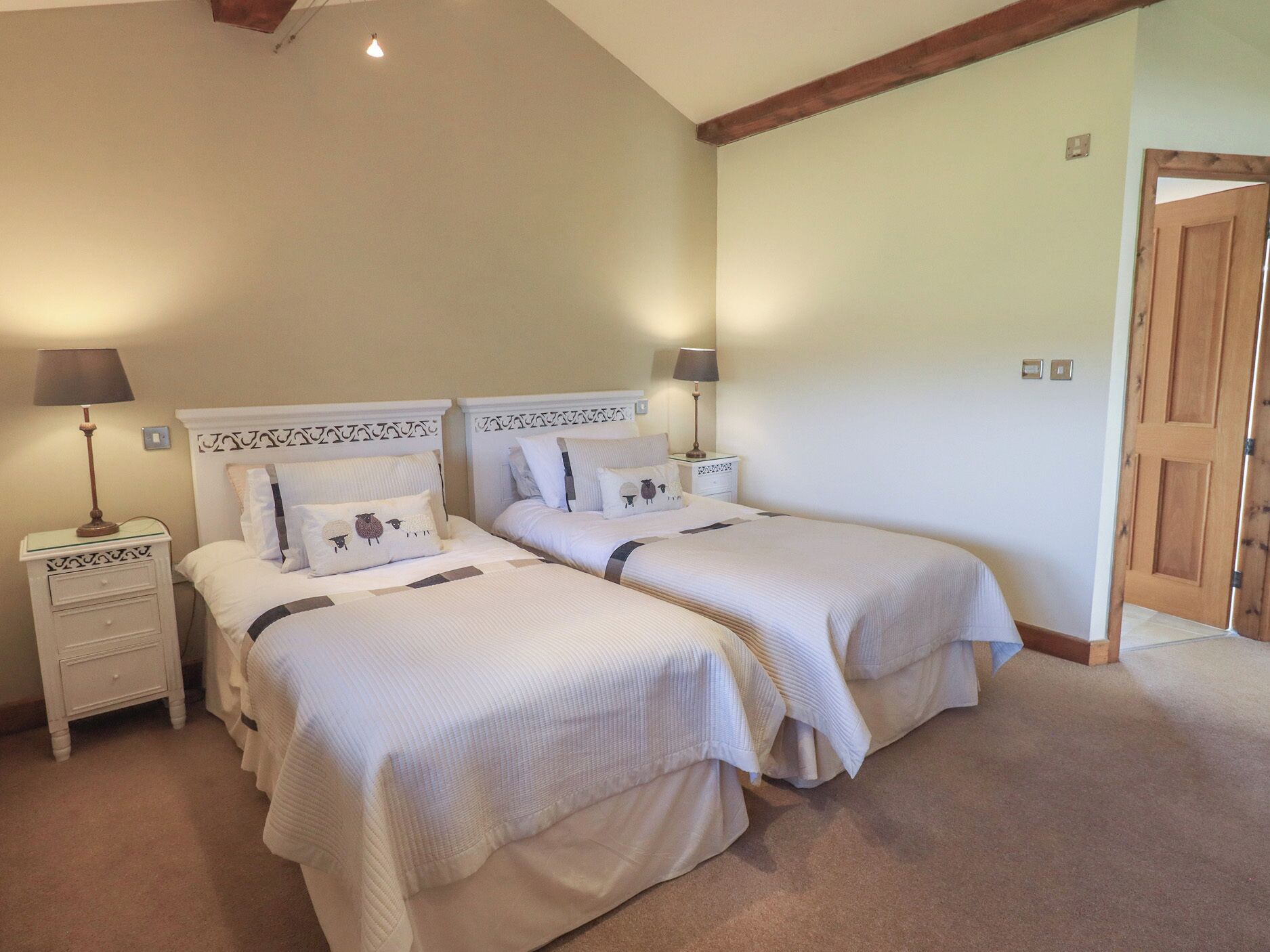 A bedroom with two beds, each with a nightstand, lamps, and decorative pillows.