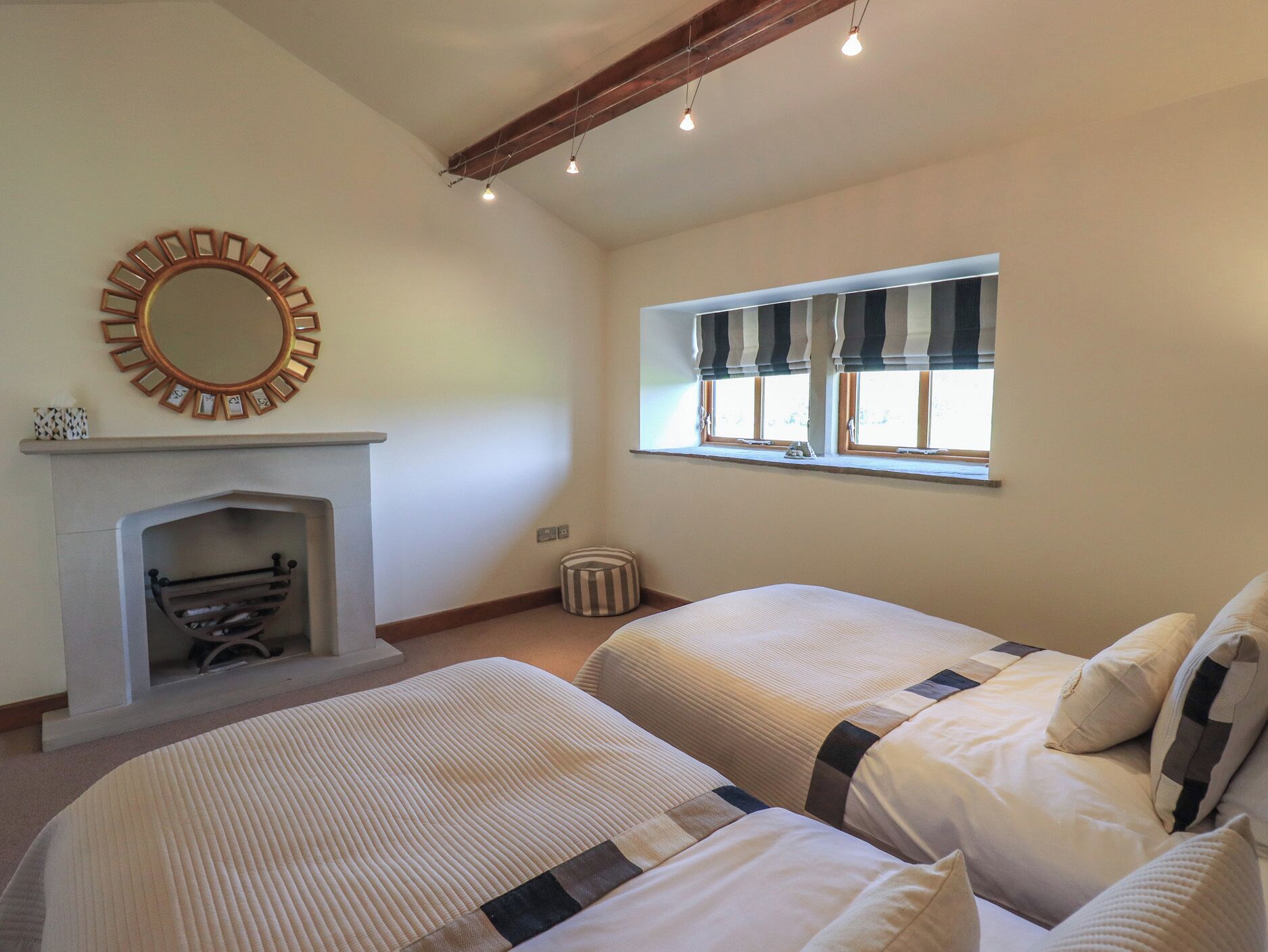 Un dormitorio con dos camas, una chimenea, un ventanal con cortinas a rayas y un espejo en la pared.