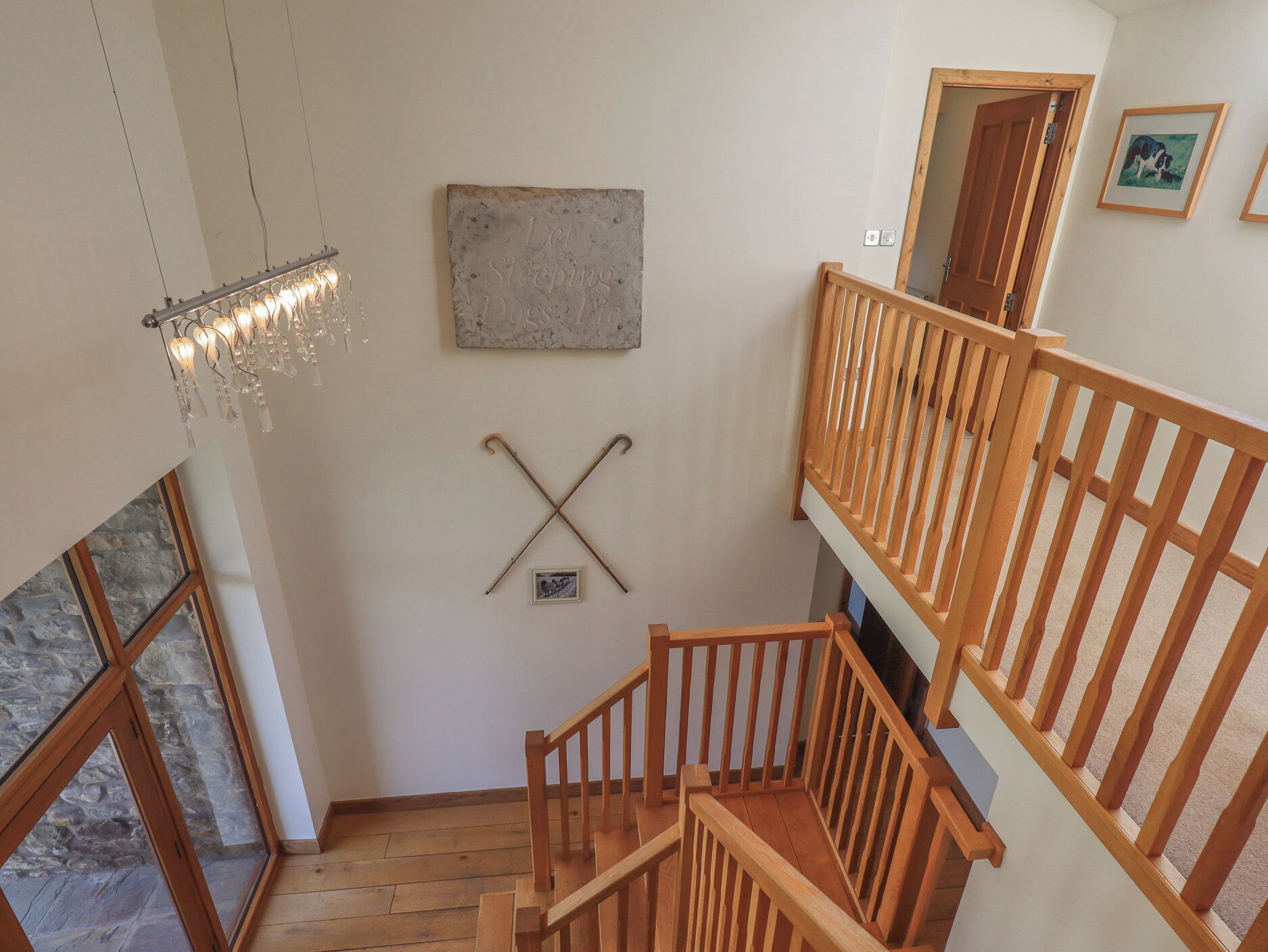 A wooden staircase with a railing, a chandelier, and a wall-mounted picture frame.