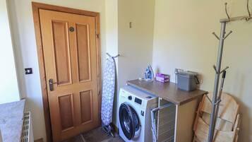 A laundry room with a washing machine, a drying rack, a coat rack, and a door.