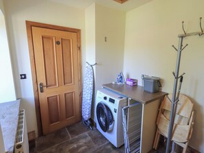 A laundry room with a washing machine, a drying rack, a coat rack, and a door. - Shepherd's Barn (Lancaster)