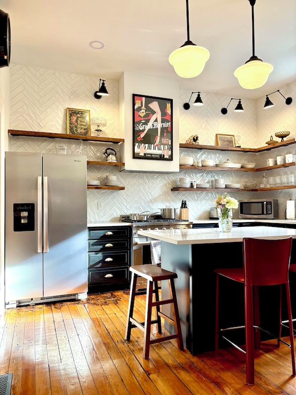 A modern kitchen with a refrigerator, microwave, stove, and wooden flooring.