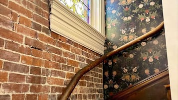 Back stairs off the kitchen — stained glass, exposed brick, and botanical wallpaper the whole way up