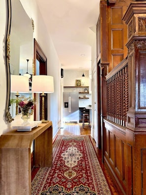 A hallway with a wooden floor, a red patterned rug, a wooden bench, and a mirror with a vase of flowers. - Middle Manor | Sleeps 8, with parking | 5mi to Pgh (Pittsburgh)