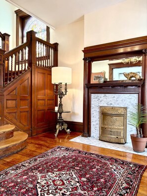 A grand staircase with wooden railings and a chandelier, leading to a room with a fireplace and a large rug. - Middle Manor | Sleeps 8, with parking | 5mi to Pgh (Pittsburgh)