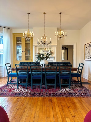 A dining area with a wooden table, six chairs, a chandelier, and a patterned rug.