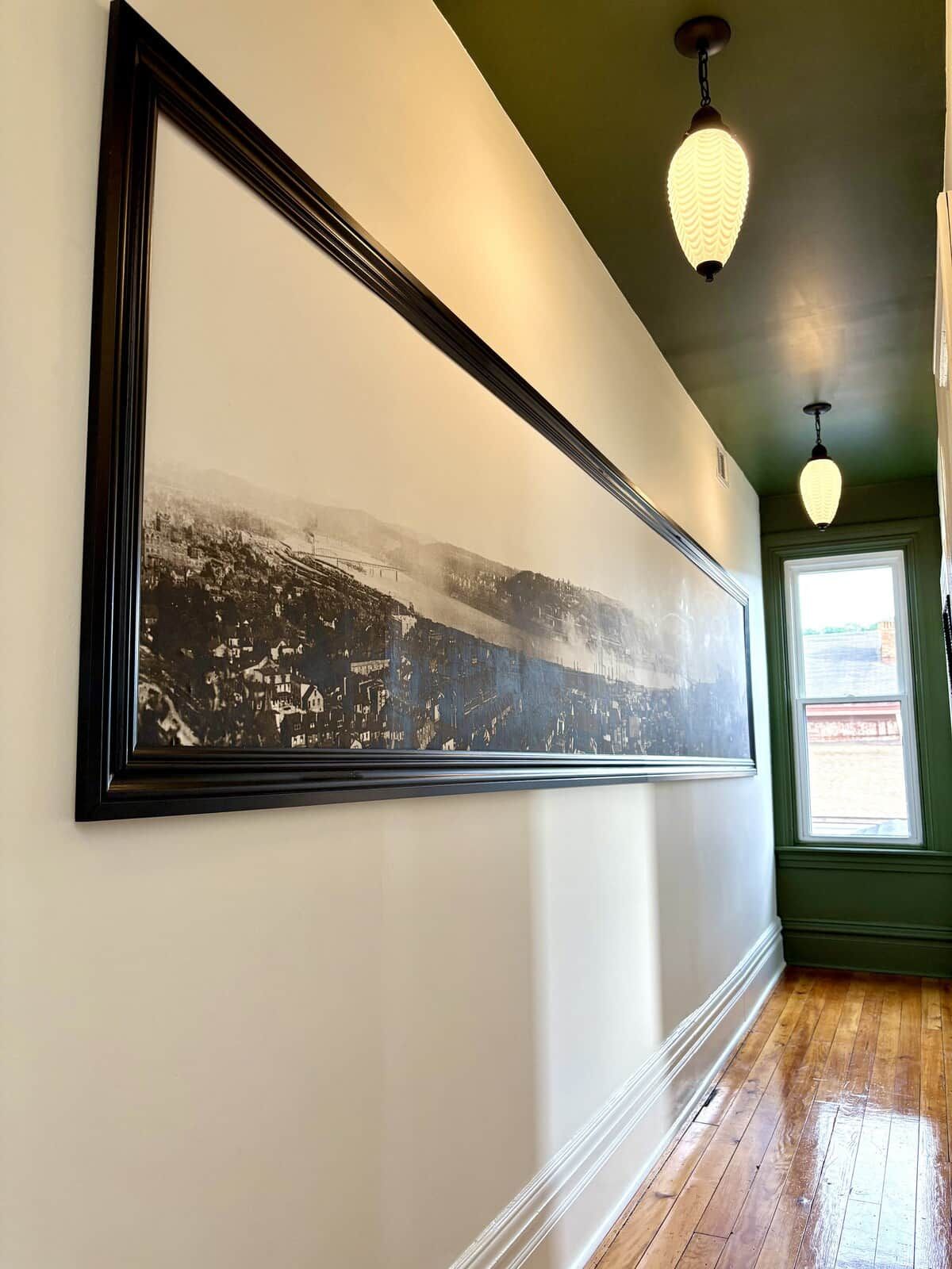 Ein Flur mit einem in Schwarz-Weiß gerahmten Foto an der Wand, Holzboden und Pendelleuchten.