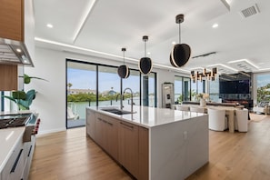A modern kitchen with a large island, a dining area with a TV, and a view of the sea. - Luxury waterfront home: dock, pool, spa, golf sim (Indian Rocks Beach)