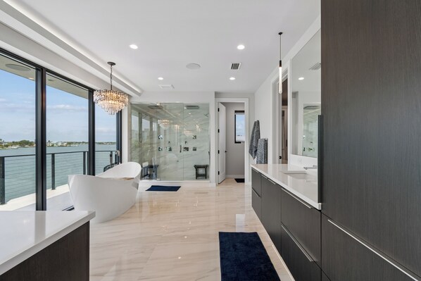 A modern bathroom with a large bathtub, a glass shower enclosure, and a view of the water. - Luxury waterfront home: dock, pool, spa, golf sim (Indian Rocks Beach)