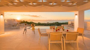 Eine Dachterrasse mit Esstisch, Stühlen und Blick auf das Meer bei Sonnenuntergang.