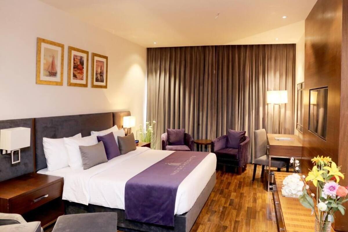 A hotel room with a large bed, two armchairs, a small table, a desk, and a TV.