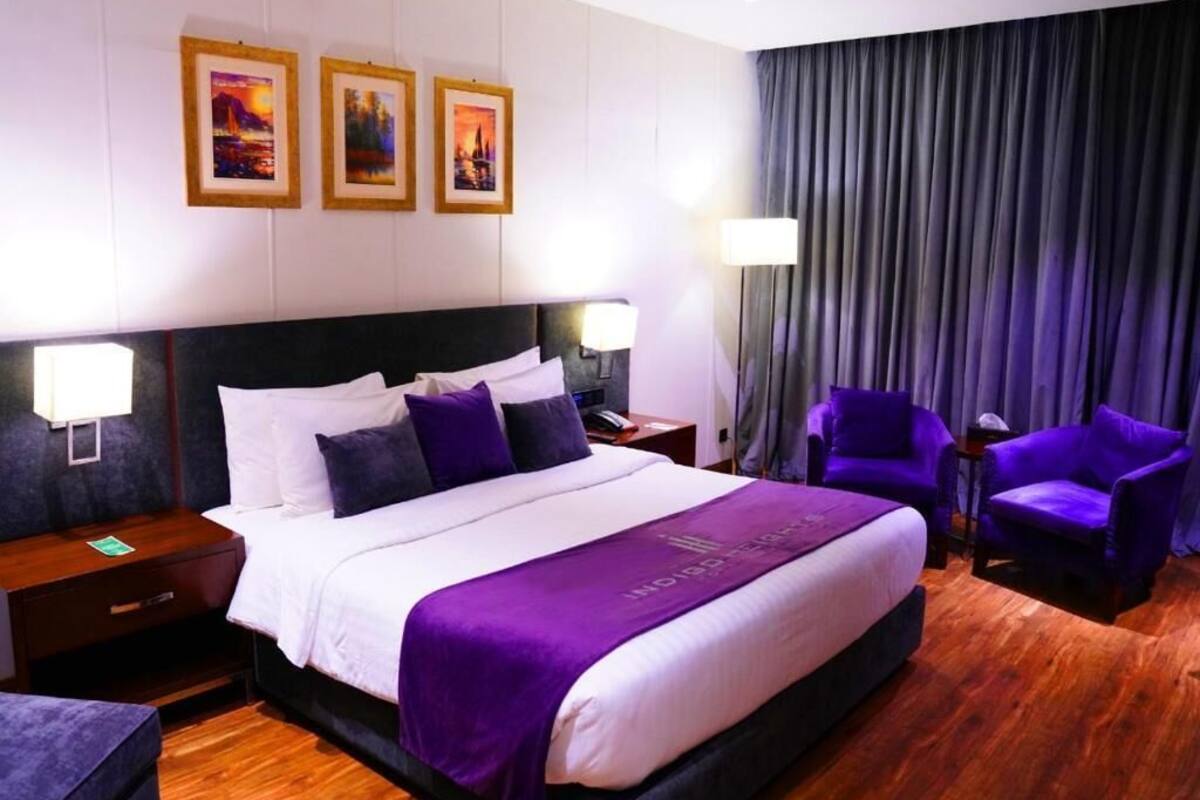 A hotel room with a large bed, two nightstands, a desk, a chair, and a view of a cityscape through the window.