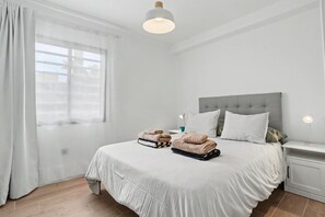 Ein Schlafzimmer mit Bett, Nachttischen, einem Fenster mit Vorhängen und einer Deckenleuchte.