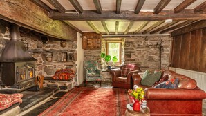 Ein rustikales Interieur mit Steinwand, Holzbalken, Kamin, Ledersofa und einem roten Teppich.