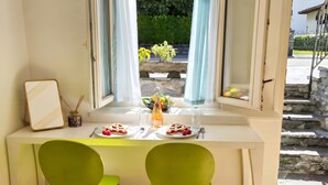 Un comedor con una mesa lista para dos, una ventana con cortinas y vistas a zonas verdes al exterior.