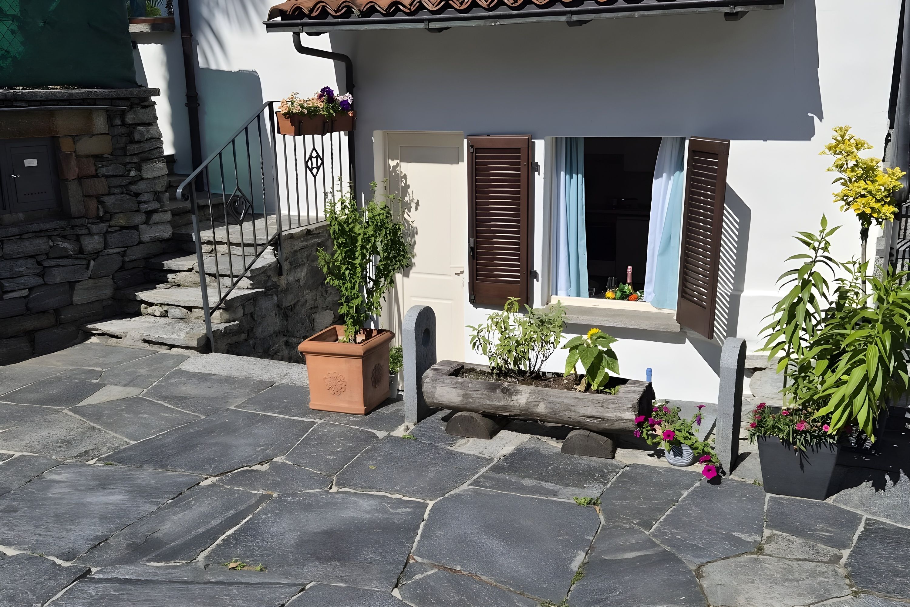 A stone-paved courtyard with a white building, wooden shutters, and potted plants.