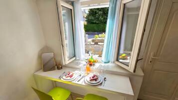 Un coin repas avec une table dressée pour deux personnes, une fenêtre avec des rideaux et une vue sur l’extérieur.