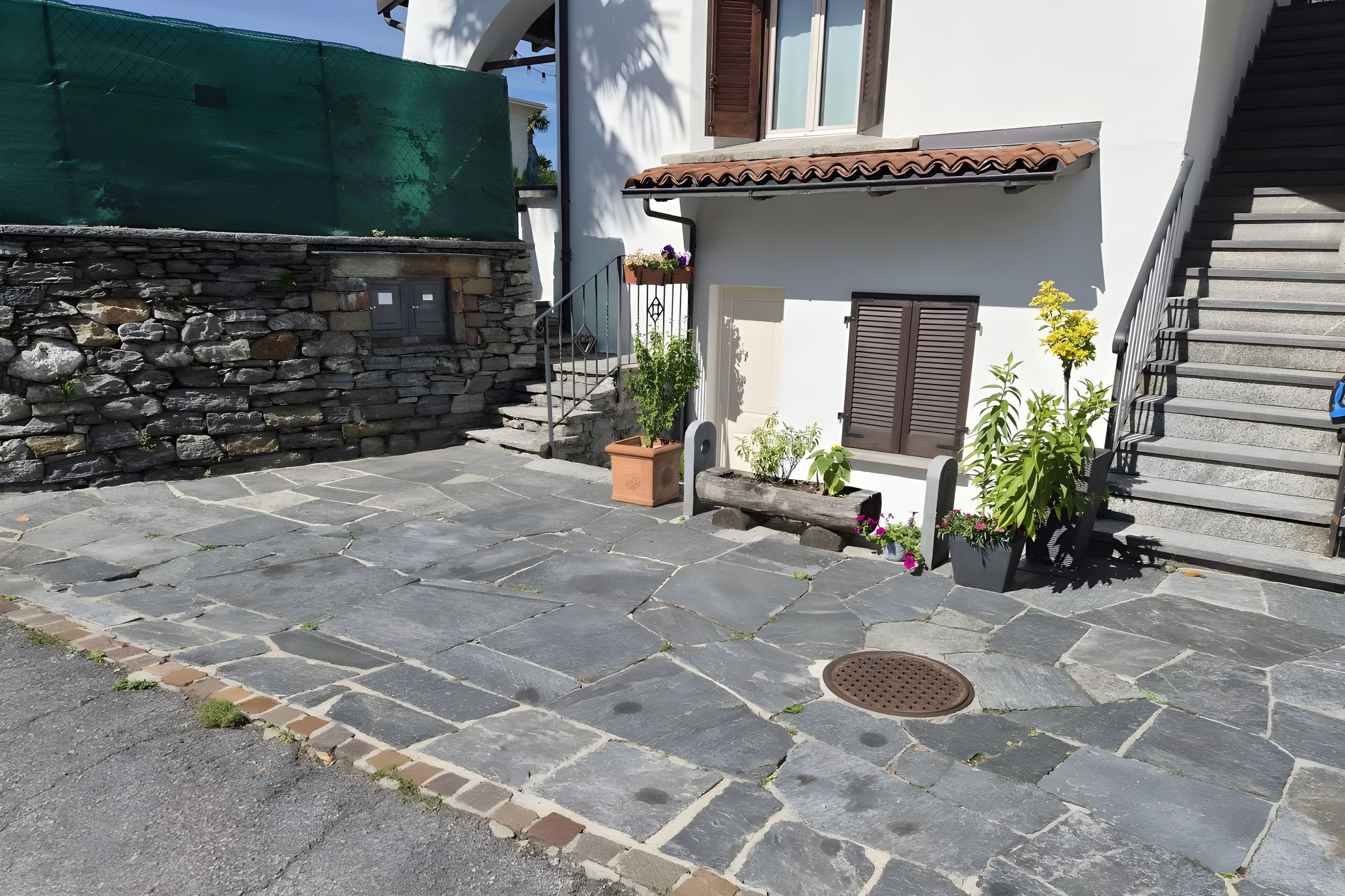 A stone-paved courtyard with a staircase, a stone wall, and potted plants.