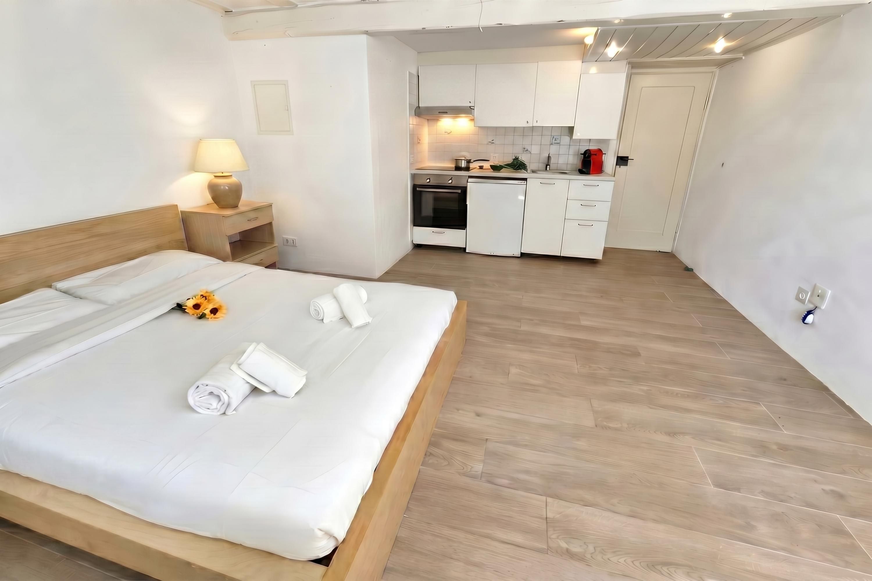 Une chambre à coucher avec un lit, une table de chevet, une lampe et une petite table ornée d’un vase de fleurs.
