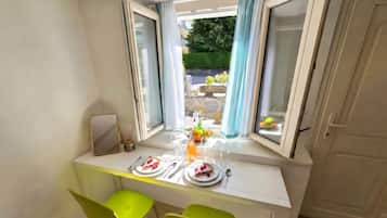 A dining area with a table set for two, a window with curtains, and a view of the outdoors.