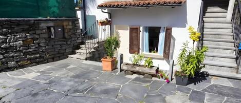 A stone-paved courtyard with a stone wall, a staircase, and potted plants.