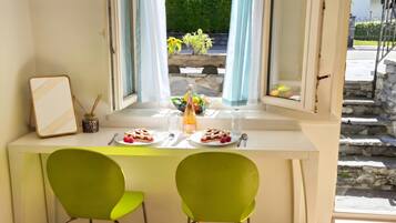 Un comedor con una mesa lista para dos, una ventana con cortinas y vistas a zonas verdes al exterior.