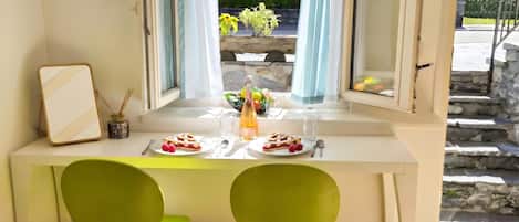 A dining area with a table set for two, a window with curtains, and a view of greenery outside.