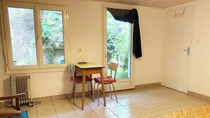 Et værelse med seng, et bord, to stole, en radiator og et vindue med udsigt til grønne områder.