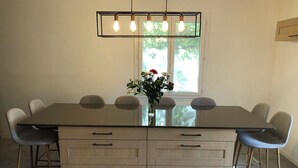 Un comedor con una amplia mesa rectangular, seis sillas, un jarrón con flores y una lámpara colgante.
