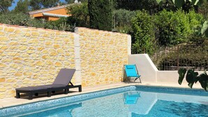 Una piscina con muros de piedra y dos sillas reclinables.