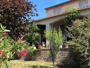 Ein zweistöckiges Gebäude mit einer Stein-Fassade, einer Veranda und einem Garten mit verschiedenen Pflanzen und Blumen.