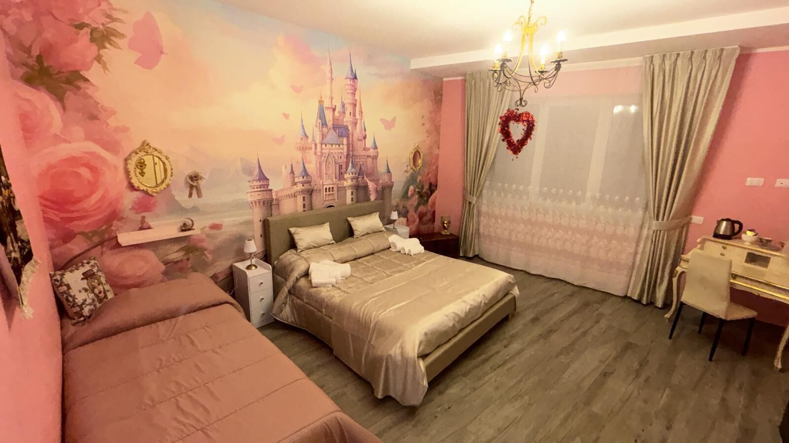A bedroom with a large bed, a desk, a chair, a nightstand, and a wall mural.