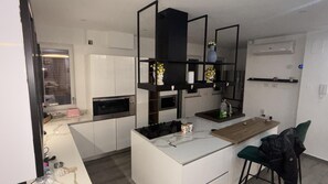 A modern kitchen with white cabinets, a built-in oven, a black countertop, and a small dining area with a chair. - Vanila Dream's House (Palermo)