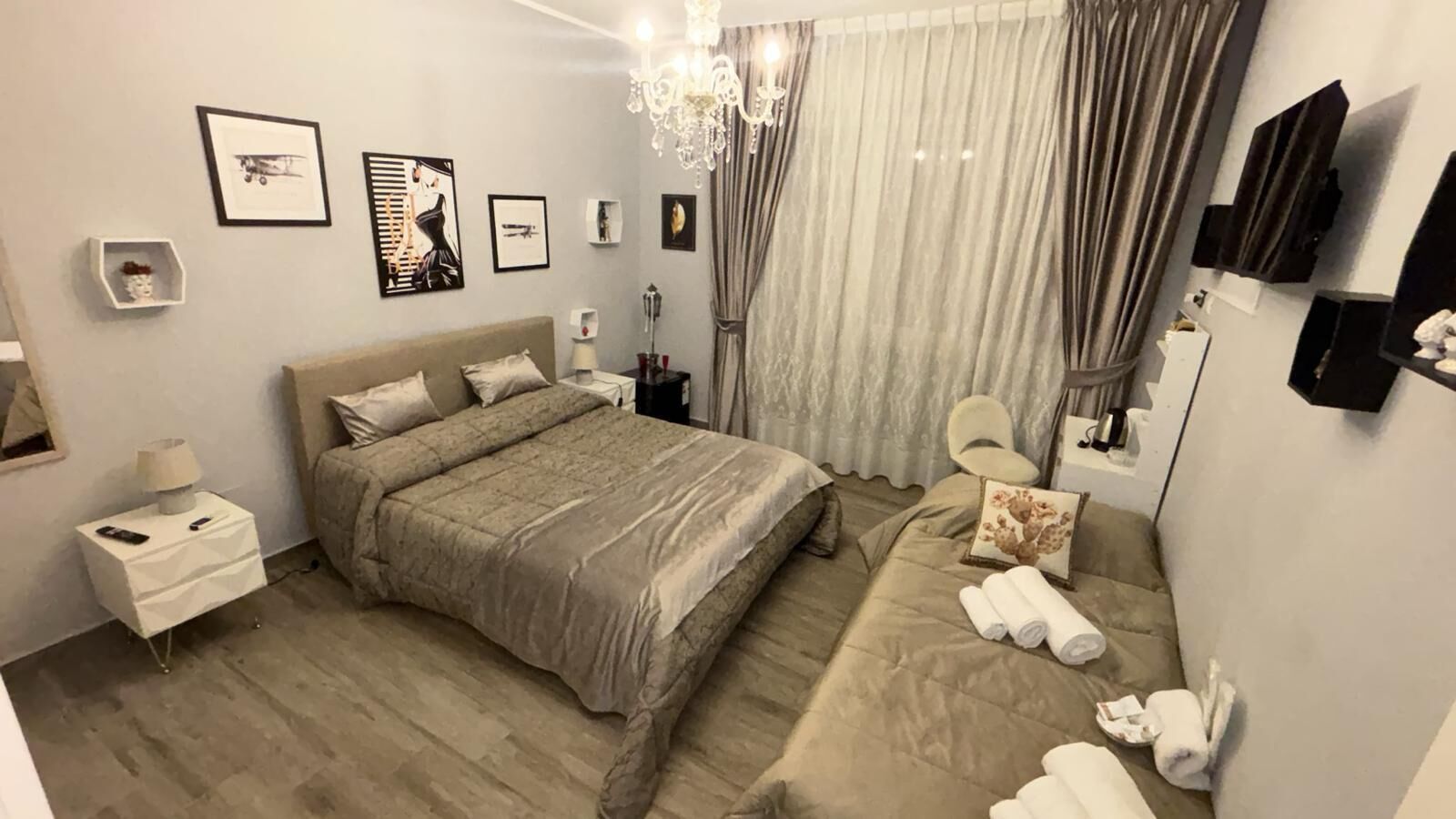 A modern bedroom with a large bed, bedside tables, a vanity, and a chandelier.