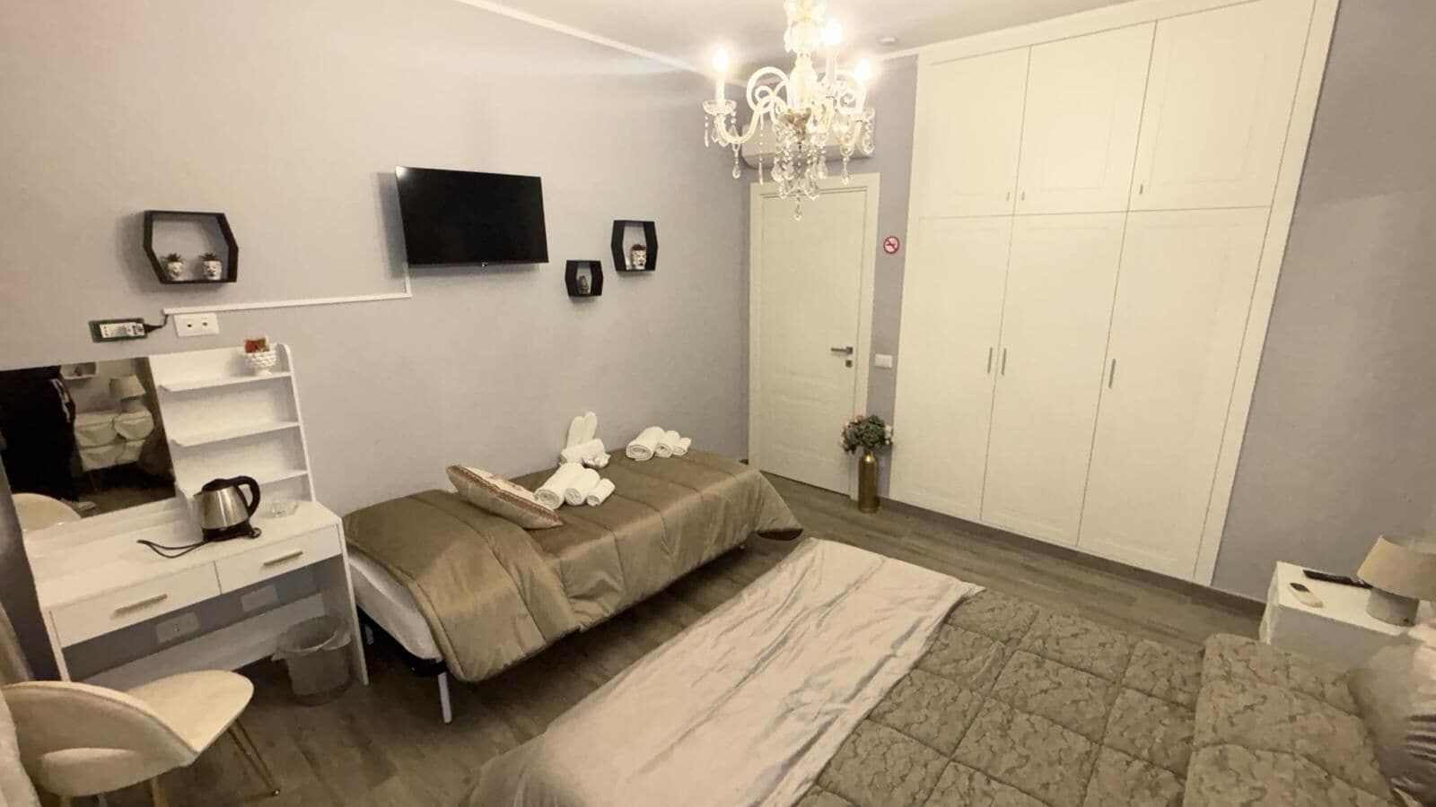 Ein Schlafzimmer mit einem Bett, einem Fernseher, einem Kleiderschrank, einer Chandelüster und einem Nachttisch.