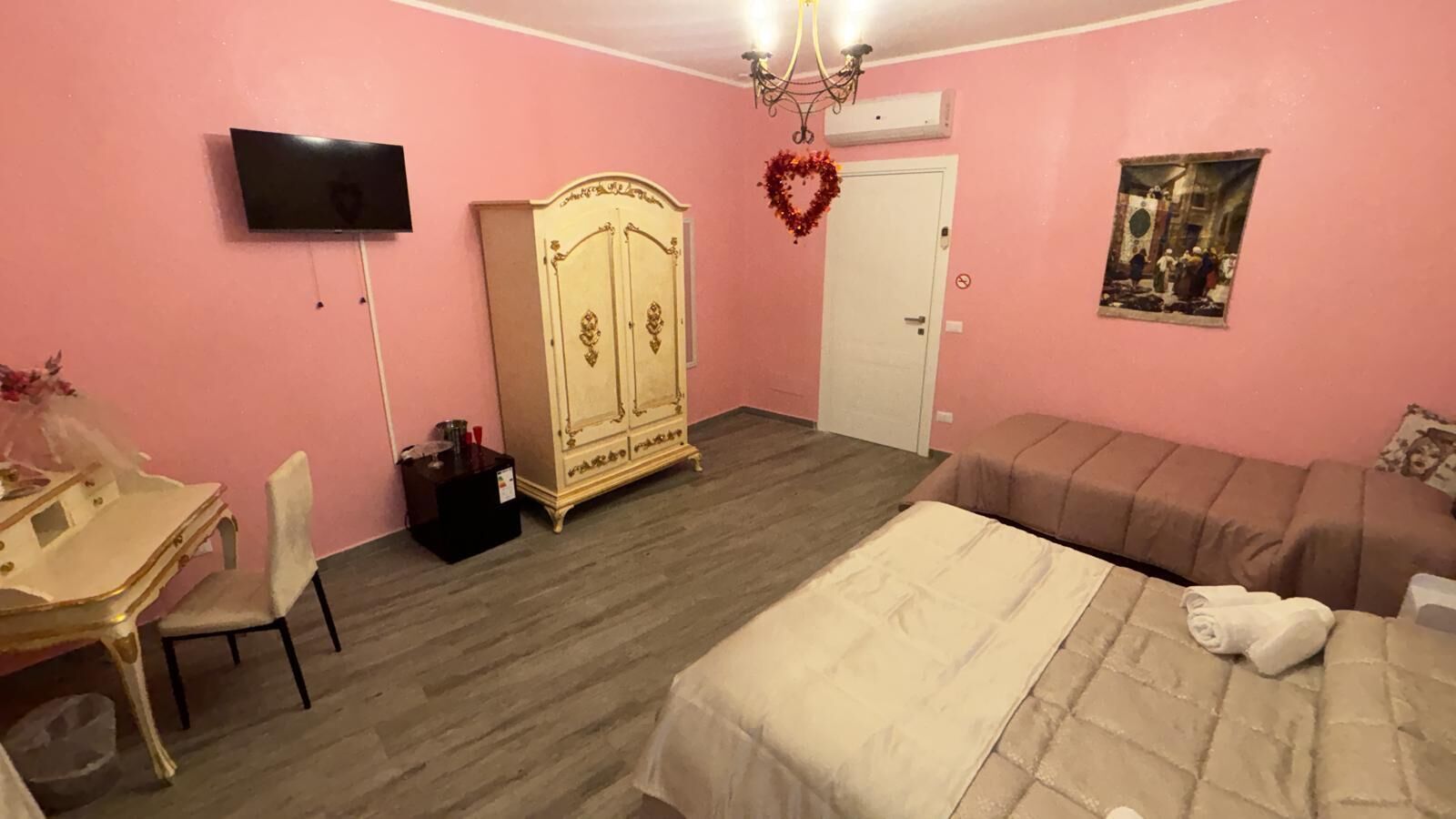 A pink-themed bedroom with a bed, a desk, a wardrobe, and a television.